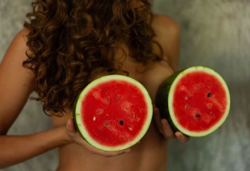 Lady holding two watermelons in front of her body to signify breasts