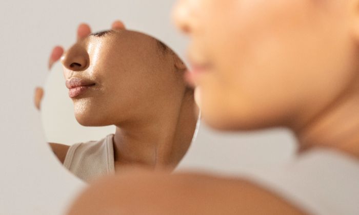 Woman examining her jawline and double chin area in the mirror.