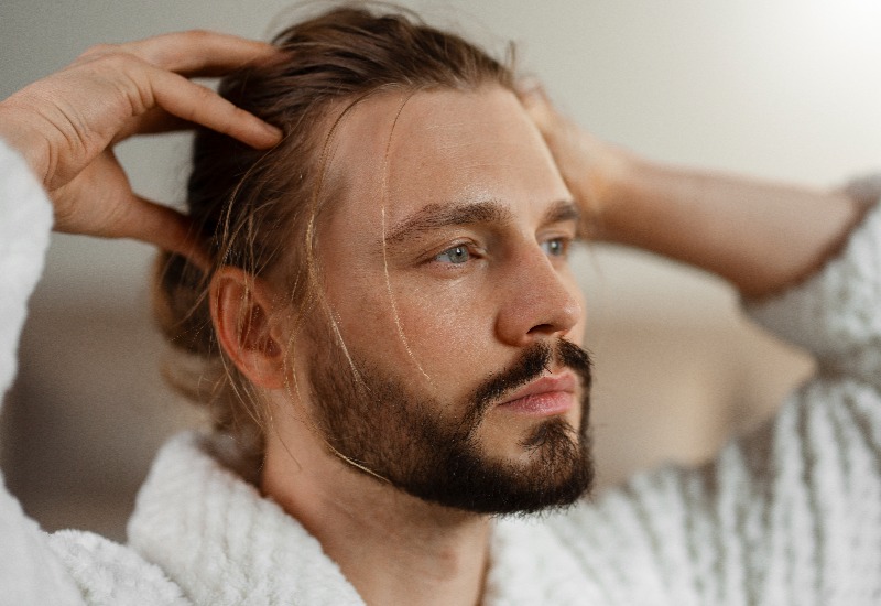 Man with beard and long hair massaging scalp. 