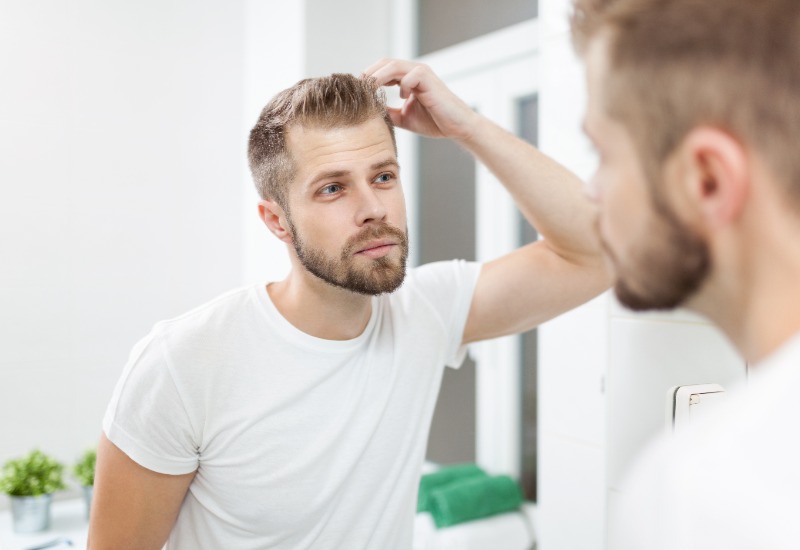 Man inspecting his hair and hairline in a bathroom mirror. 